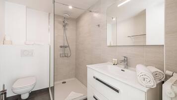 A modern bathroom with a glass-enclosed shower, a white sink with a mirror, and a toilet.
