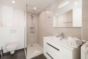 Un baño moderno con ducha de vidrio, lavamanos blanco con espejo y retrete.
