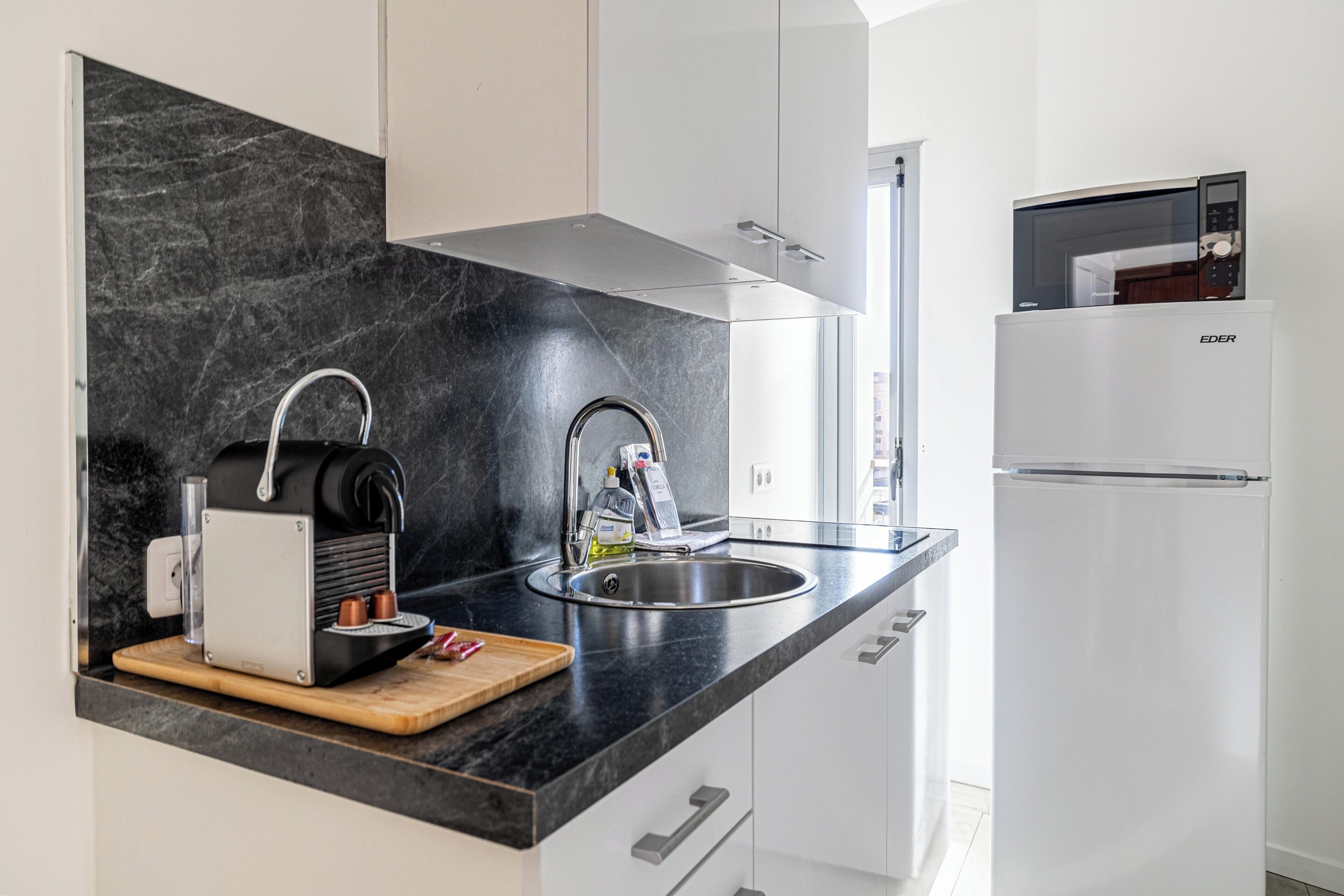 Una cucina moderna con un piano di lavoro nero, lavello in acciaio inossidabile e frigorifero bianco.