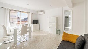 Una sala de estar moderna con comedor, un sofá, un televisor y un balcón con vista a la ciudad.