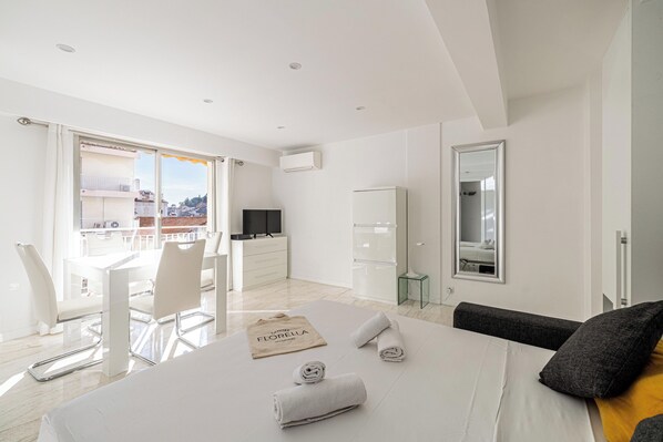A modern hotel room with a bed, a desk, a chair, a TV, and a balcony with a view.