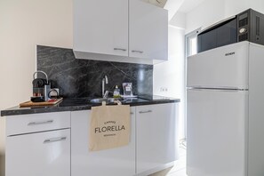 A modern kitchen with white cabinets, a black marble countertop, a coffee machine, a microwave, and a refrigerator.