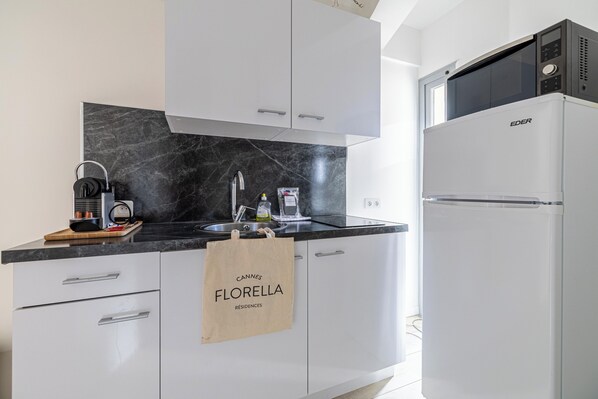 Una cocina moderna con armarios blancos, encimera de mármol negro, cafetera, microondas y refrigerador.