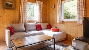 Ein Holzblockhaus-Interieur mit einer Couch, einem Couchtisch, einem Fernseher und Karottenvorhängen.