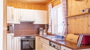 Eine Küche mit Holzausstattung, Backofen, Geschirrspüler und einem Fenster mit Vorhängen.