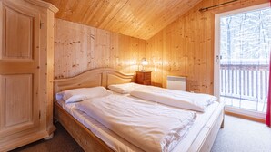 Ein Zimmer mit Holzboden, einem Bett, einem Schrank, einem Nachttisch und einem Fenster mit Blick auf Bäume.