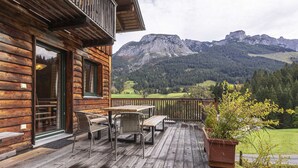 Eine Holzterrasse mit Gartenmöbeln, einem Blumentopf und Blick auf die Berge.