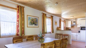 Un comedor con una mesa y sillas de madera, un jarrón con flores, y una cocina al fondo.