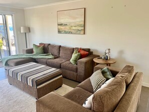 A living room with a brown sofa, a striped ottoman, and a small round table with decorative items. - Riptide - Pet friendly outside, WiFi (Robe)