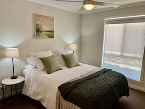 A bedroom with a bed, two bedside lamps, a window with a view, and a ceiling fan. - Riptide - Pet friendly outside, WiFi (Robe)