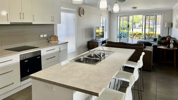 A modern kitchen with white cabinets, a central island with a sink, pendant lighting, and a view to the outdoor patio.