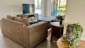 A living room with a sofa, a TV, a sliding glass door, and a small table with a plant.