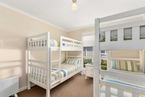 Une chambre d’enfant avec des lits superposés, une commode et une fenêtre avec des stores.