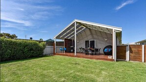 A covered outdoor area with a table and chairs, a grill, and a wooden fence.