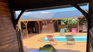 An outdoor deck with a pool, wooden furniture, and a covered area with a view of the mountains.