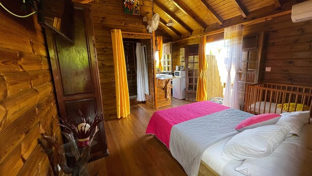 A wooden cabin room with a bed, a desk, and a kitchenette.