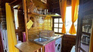 A rustic kitchen with wooden walls, a sink, a washing machine, and a fan.