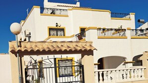 Un edificio de dos pisos con fachada blanca, detalles en amarillo y una entrada con reja.