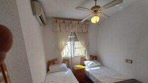 Una habitación pequeña y limpia con dos camas individuales, un ventilador de techo y una ventana con cortinas.