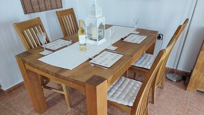 Una mesa de madera con cuatro sillas, una botella de vino blanco, una vela y un menú.