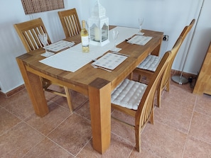 A wooden dining table with four chairs, a bottle of white wine, a candle, and a menu.