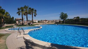 Una piscina grande y cristalina de color azul con borde de azulejos, rodeada de palmeras y una cerca.
