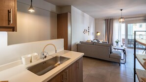 Una cocina moderna con un lavamanos integrado y armarios de madera, un comedor con mesa y sillas, y una sala de estar con sofá y lámpara.