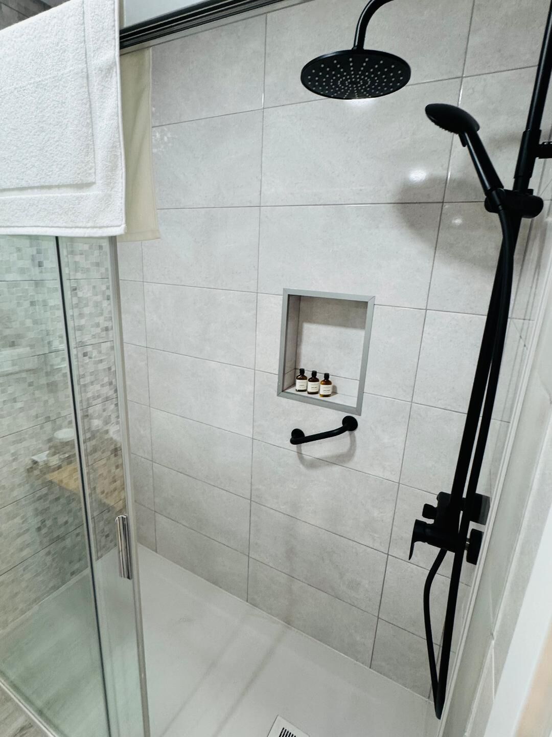 A modern shower area with a glass door, a handheld showerhead, and a handheld shower attachment.