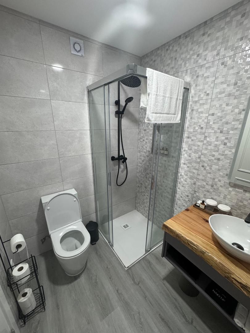 A modern bathroom with a glass-enclosed shower, a toilet, and a wooden vanity with a sink.