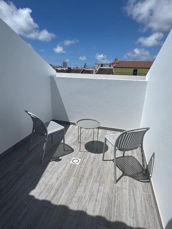 A rooftop terrace with two metal chairs and a small glass table, featuring a clear view of the city skyline.