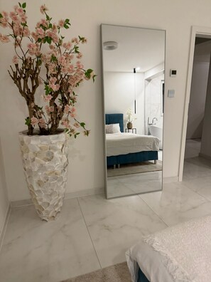 A bedroom with a large mirror, a potted plant, and a bed with a blue headboard. - Luxrem Apartments 4  (Biel)