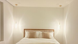 Une chambre à coucher au style minimaliste, avec un grand lit, deux lampes de chevet et un luminaire au plafond.