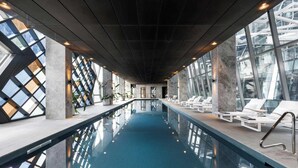 An indoor swimming pool with clear glass walls, lounge chairs, and a modern architectural design. - Luxury 2BR Apt Opposite Southern Cross (Melbourne)