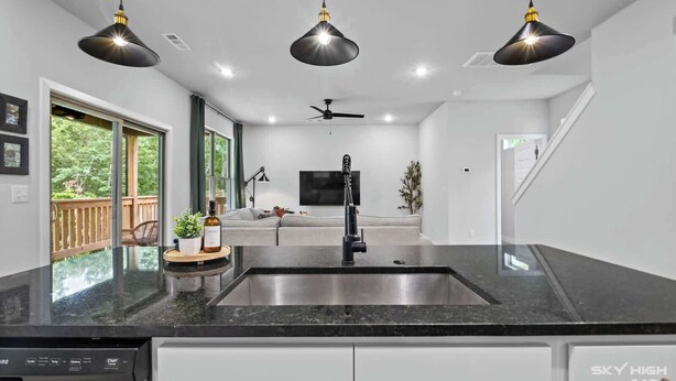 A modern kitchen with a central island, black pendant lights, a built-in dishwasher, and a view of the outdoors. - Trailside Home | Back 40 + OZ Trails Access (Bella Vista)