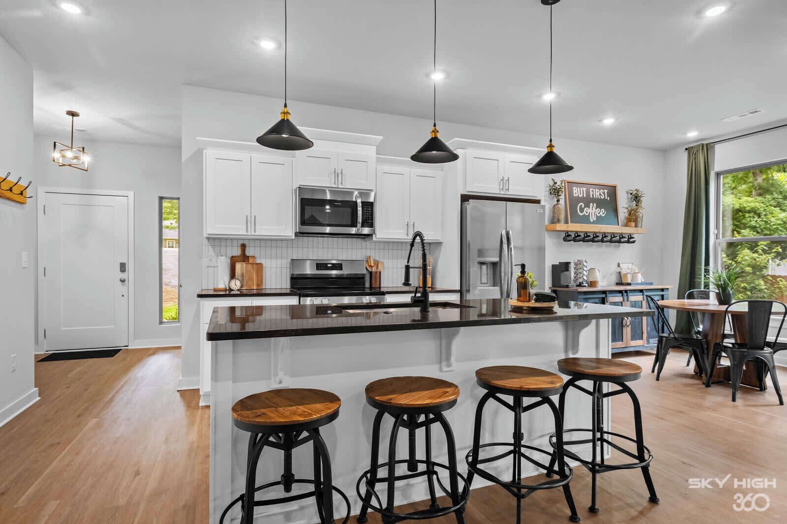 Una cocina moderna con armarios blancos, una isla central con taburetes e iluminación colgante.