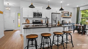 A modern kitchen with white cabinets, a central island with stools, and pendant lighting. - Trailside Home | Back 40 + OZ Trails Access (Bella Vista)