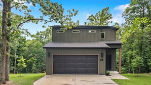 A two-story building with a garage, surrounded by trees. - Trailside Home | Back 40 + OZ Trails Access (Bella Vista)