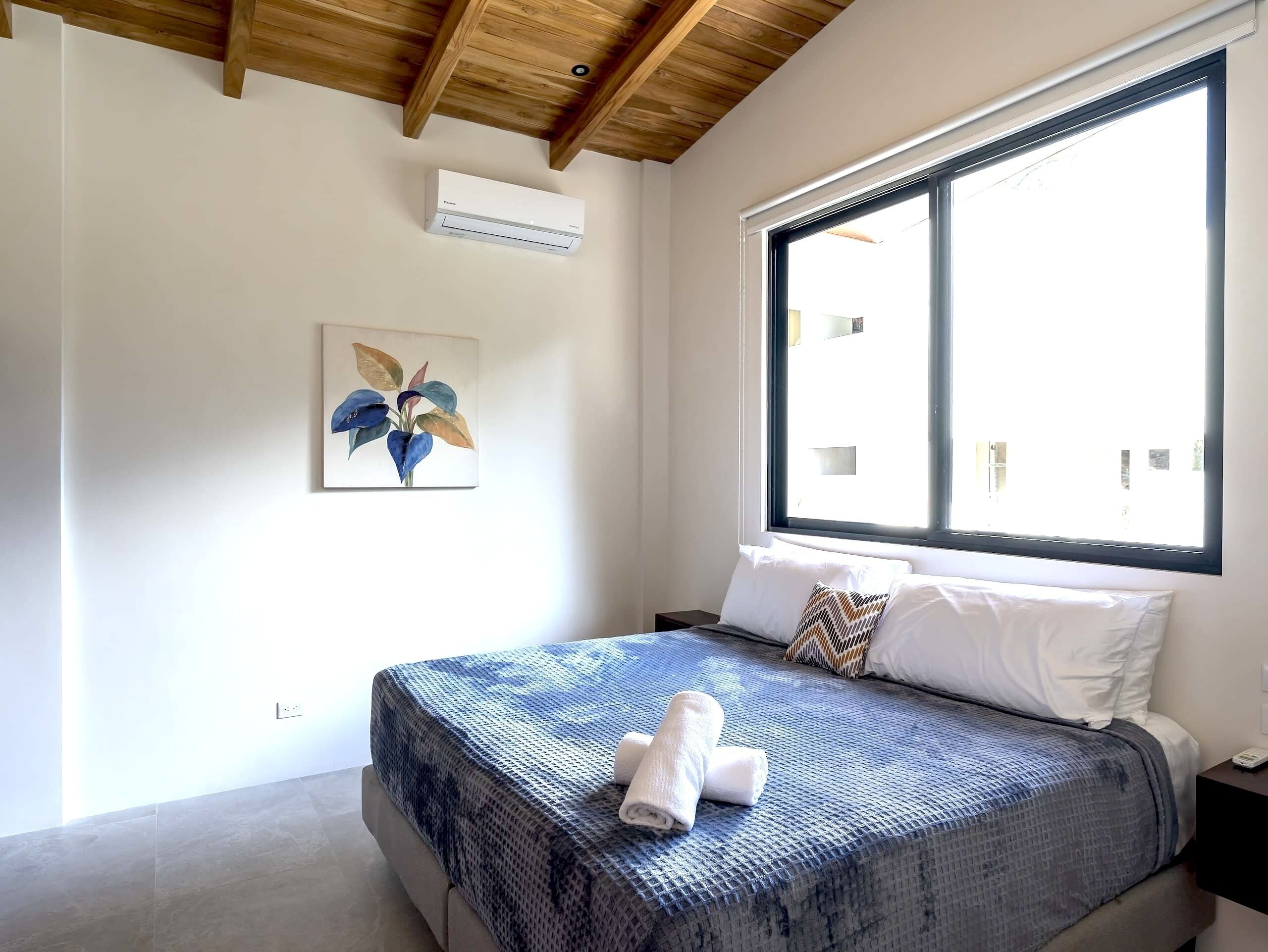 A bedroom with a bed, a window, a ceiling fan, and a wall-mounted air conditioner.