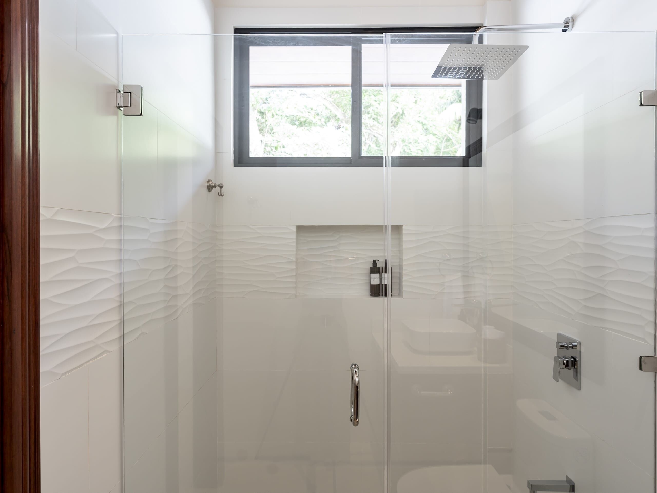 A modern bathroom with a glass shower enclosure, a window, and a textured wall design.