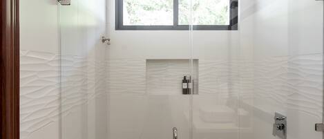 A modern bathroom with a glass shower enclosure, a window, and a textured wall design.