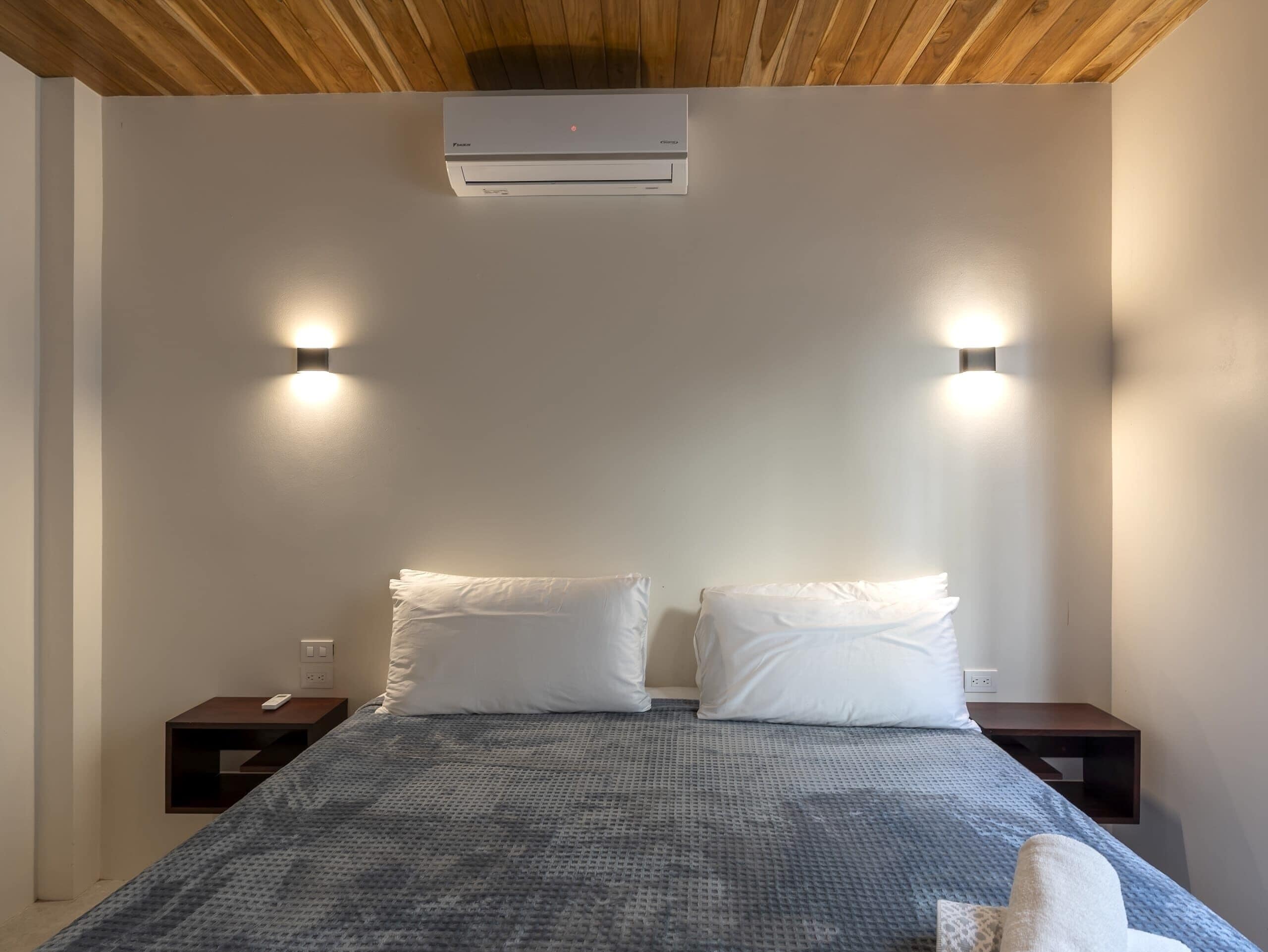 Una camera da letto con un letto, due comodini, un condizionatore d'aria a parete e due luci a parete.