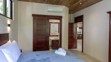 A hotel room with a bed, a wooden ceiling, a bathroom with a sink, and a view of the outside.