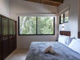 Un dormitorio con un ventanal grande, una cama con ropa de cama blanca y un armario de madera.