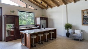 Une cuisine moderne dotée d’un grand îlot central, de tabourets de bar, d’un réfrigérateur et d’une fenêtre donnant sur la verdure.