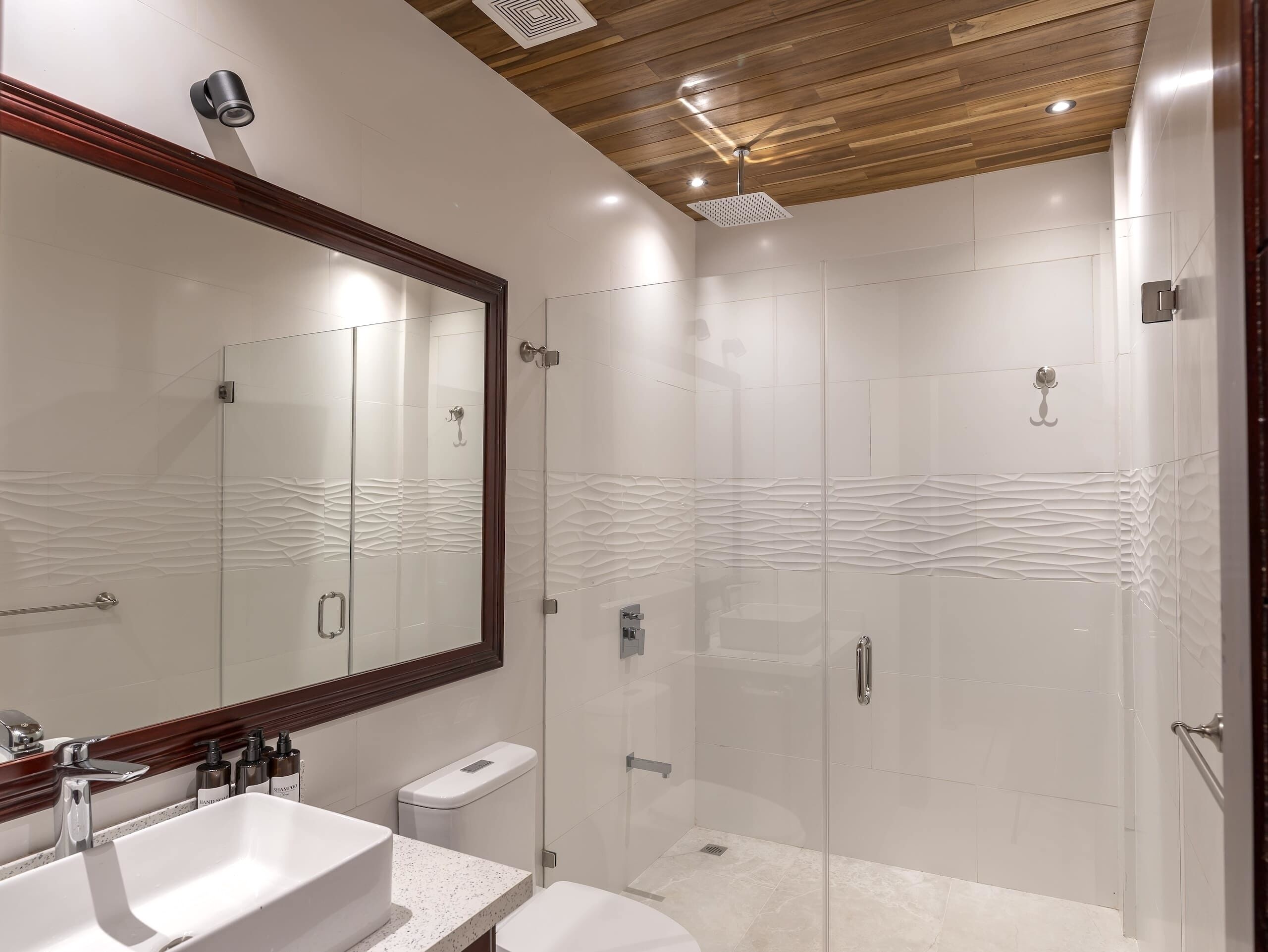 Un baño moderno con un espejo grande, un lavamanos, un inodoro y una zona de ducha.