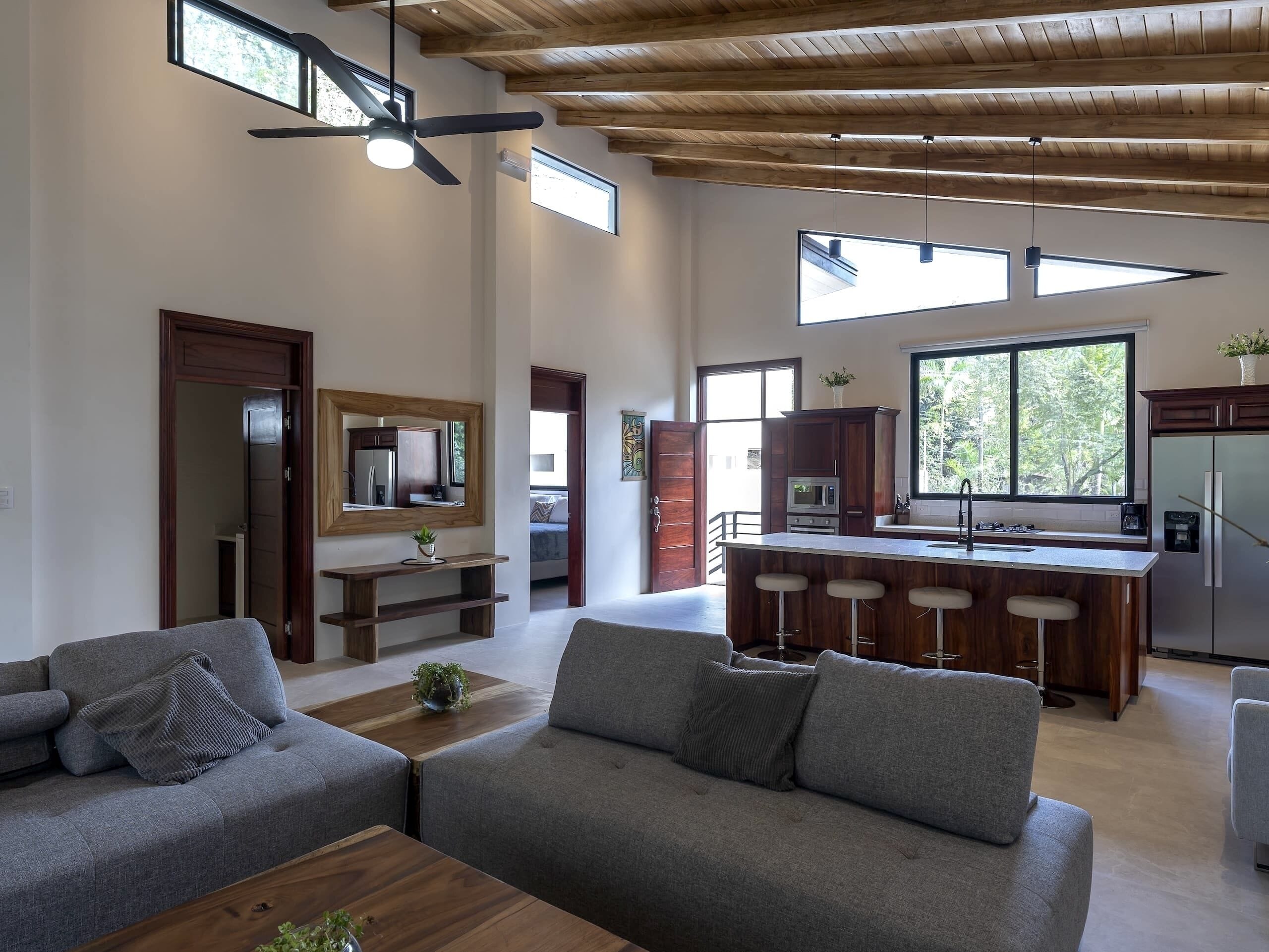 A spacious living area with a gray sofa, wooden coffee table, and a kitchen with a bar.
