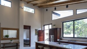 Une cuisine moderne dotée d’un grand îlot central, de tabourets de bar, de meubles en bois et offrant une vue sur l’extérieur.