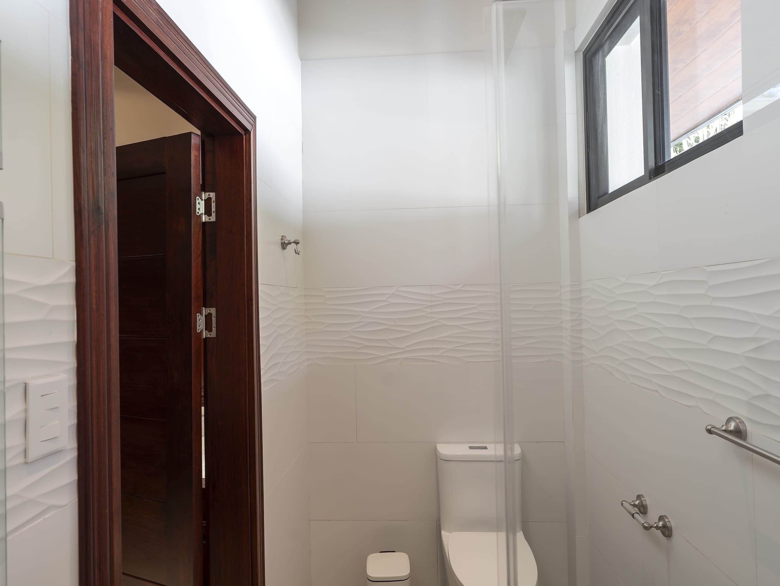 Une petite salle de bain avec des toilettes blanches, une porte en bois et une cabine de douche en verre.