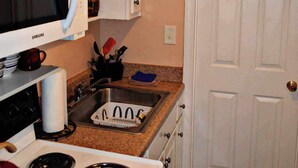 Una cocina compacta con armarios blancos, un microondas, una estufa y un lavamanos.