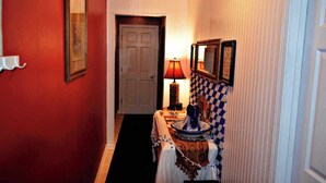 Un pasillo con pared roja, una puerta blanca y un patrón de pared a cuadros. Hay una mesa con una lámpara y un jarrón.